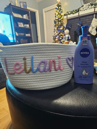 Customer's personalized white basket with 'Leilani' in colorful yarn and a heart, next to a lotion bottle for scale.