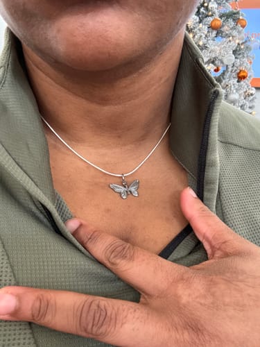 Close-up of a reviewer wearing the 1.5MM STERLING SILVER SNAKE CHAIN on their neck, paired with a butterfly pendant.