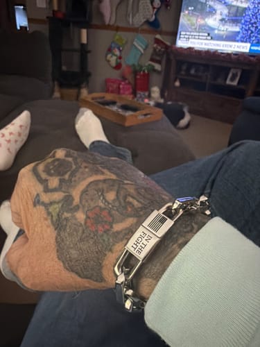 Customer wearing the steel In The Fight-Never Surrender Bracelet on a tattooed arm while relaxing.