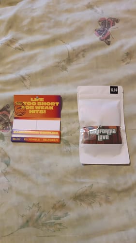 Customer's packaging for California Love THCA Flower, showing the white branded pouch on a bedspread.