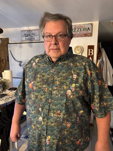 Customer wearing the dark, patterned Disney and Pixar Up 'I Found the Snipe' shirt indoors.