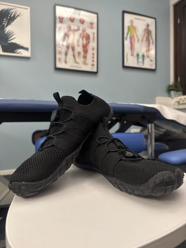 Asiakkaan mustat Vapauta Varpaat™ Paljasjalkakengät pöydällä hoitohuoneessa.