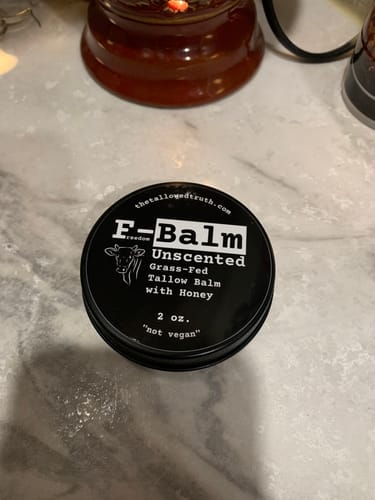 Customer's F-Balm Unscented Tallow Balm in its round, black tin, shown on a marble surface.
