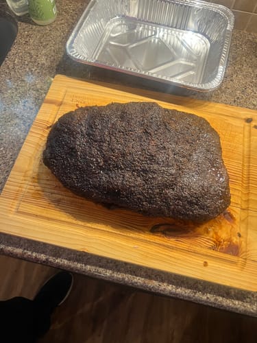 Customer's cooked USDA Prime Brisket with a dark bark, resting whole on a wooden cutting board before slicing.