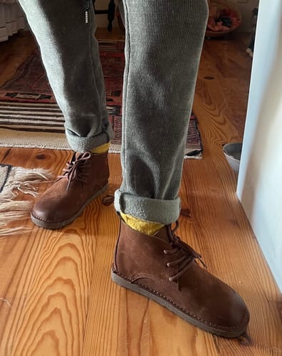 Customer wearing the brown vintage flat ankle boots with cuffed grey pants on a wood floor.
