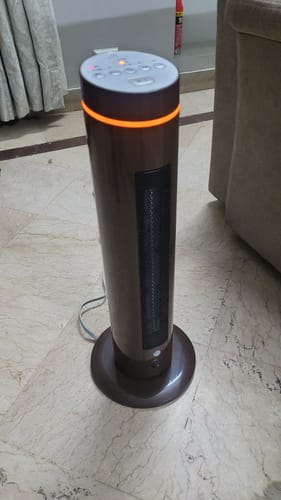 Reviewer's brown Slim Ceramic Blower Fan Heater powered on, showing a glowing orange light around the top.