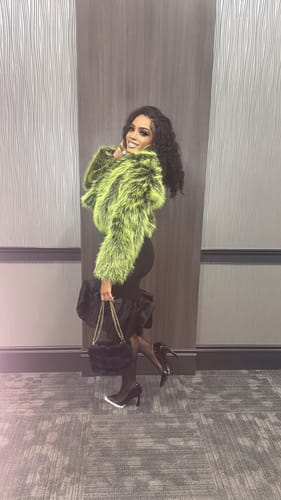 Reviewer posing indoors, wearing the vibrant green Faux Fur Straight Jacket with a black dress and heels.