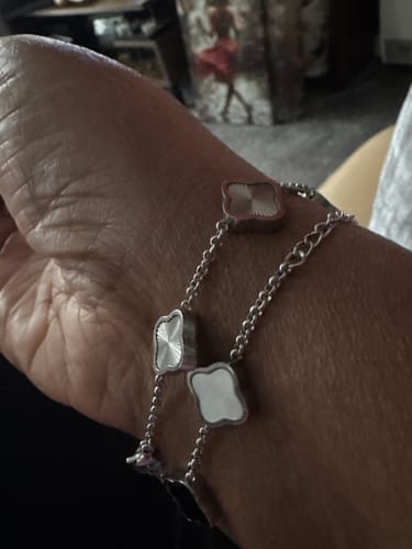 Close-up of a reviewer's wrist wearing two stacked Celine Silver Clover Bracelets.
