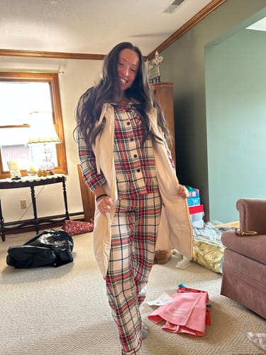 Reviewer smiling while wearing the open Falling Leaves Long Puffer Vest over a set of plaid pajamas indoors.