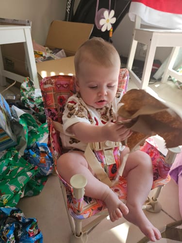 Customer's baby sitting in the bold, patterned Amy baby chair v2 at home, secured by the harness.