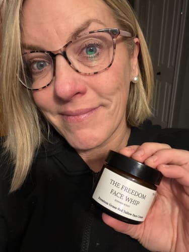 Close-up of a smiling reviewer holding the amber jar of The Freedom Face Whip.
