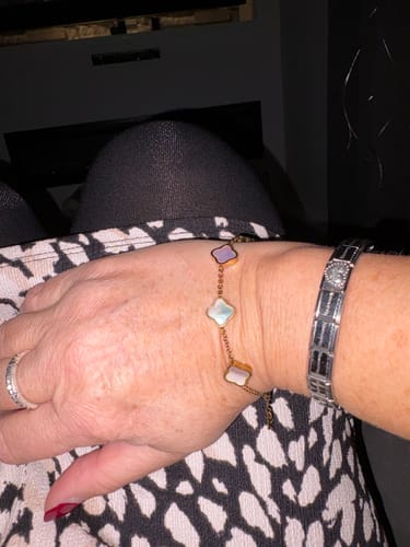 Customer's wrist wearing a delicate gold-chain bracelet with mother-of-pearl clover-shaped charms.