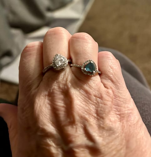 Customer showing two heart-shaped rings on their hand, one clear and one blue.