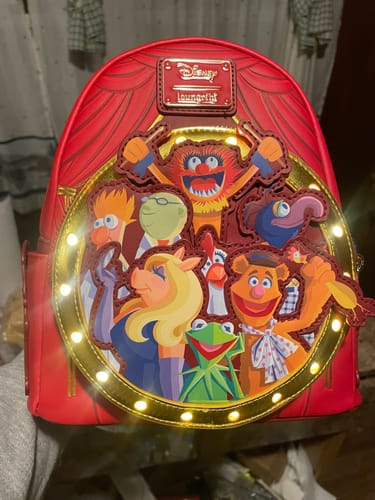 Reviewer's red Loungefly Muppets mini backpack with the bright light-up feature turned on around the front pocket.