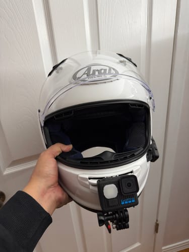 Customer holding a white Arai helmet, showing the Arai Contour-X Camera Mount with an action camera attached to the chin.
