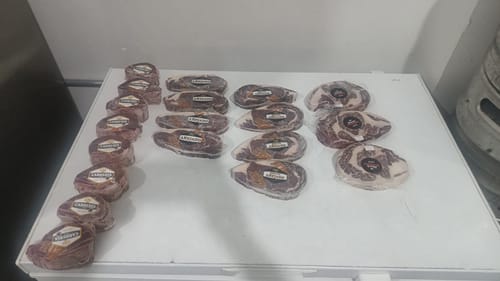 Cliente muestra varios filetes New York Steak Dry Aged y otros cortes envasados al vacío sobre un congelador.