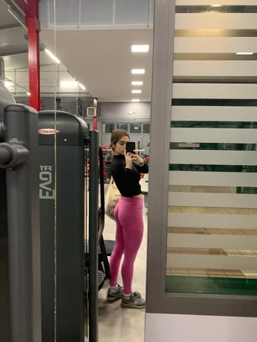 Cliente mostra la vestibilità dei Leggings Push Up Pulsar Fuxia con un selfie di profilo in palestra.