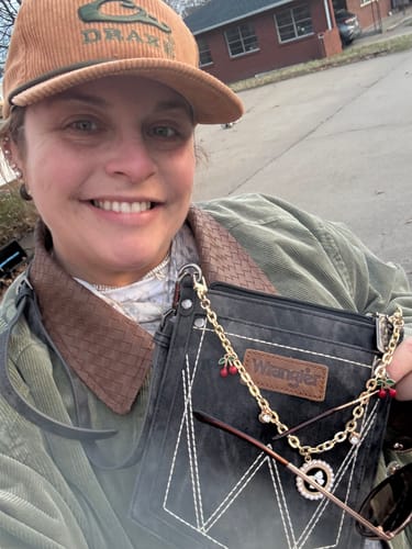 Reviewer smiling outdoors while holding their stylish Black Wrangler Pocket Style Crossbody Bag.