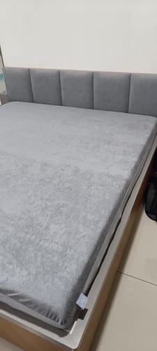 Customer's grey Flo Mattress Protector fitted onto a bed with a matching grey tufted headboard.