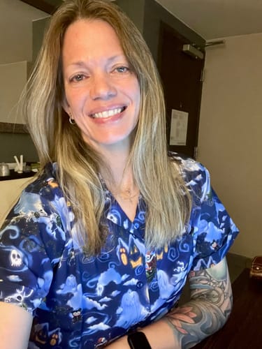 A reviewer smiling while wearing the blue, patterned "Here Comes Sandy Claws" shirt indoors.