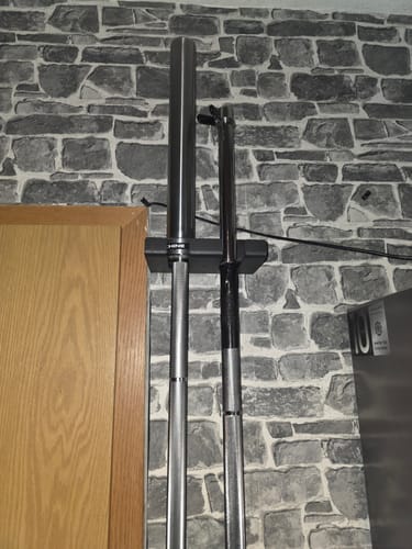 Kunde zeigt den montierten Barbell Hook an einer Steinwand, der zwei Langhanteln vertikal hält.