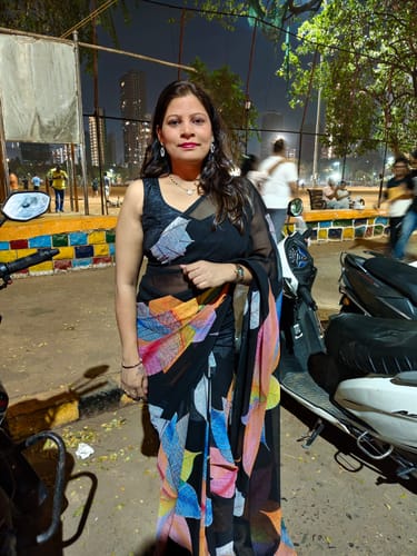 Reviewer standing outdoors at night, wearing the black printed georgette ready-to-wear saree with a colorful pattern.