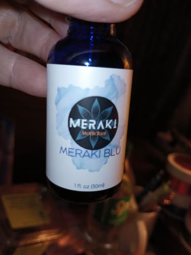 Close-up of a reviewer holding the small, blue bottle of Meraki Blu.