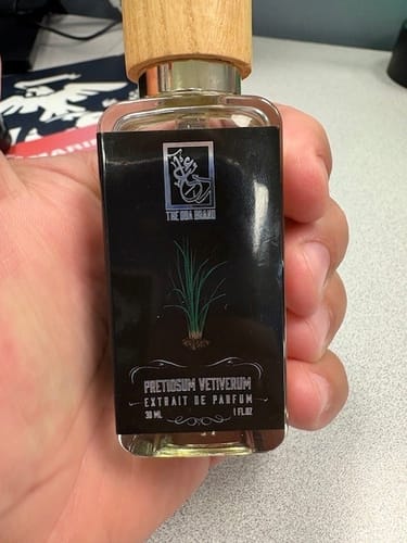 Customer holding a bottle of Pretiosum Vetiverum perfume, showing its black label and light wood cap.