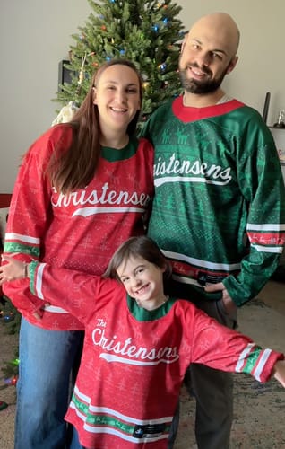 A reviewer's family wearing matching red and green Family Christmas Custom Hockey Jerseys by a tree.