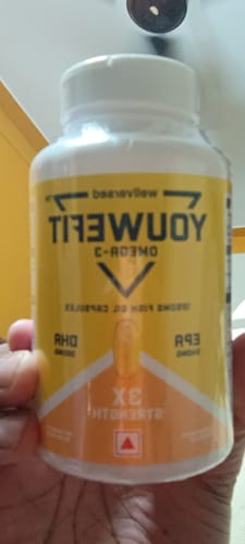 A reviewer holding a sealed white bottle of YouWeFit Omega-3 fish oil with a yellow and orange label.