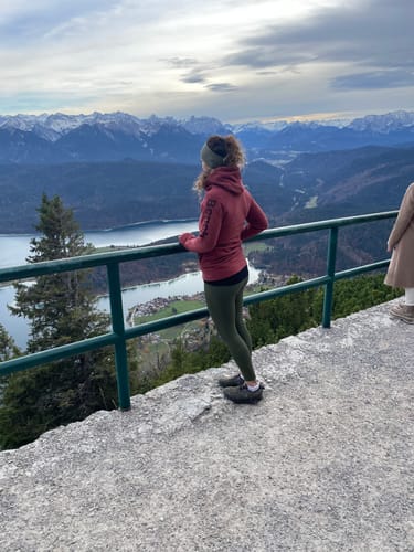 Kundin trägt die grüne Tofana Leggings, während sie von einem Berg auf einen See blickt.