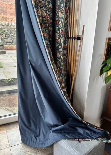 A customer's dark blackout thermal lining fabric sewn to a patterned curtain, hanging near a window.