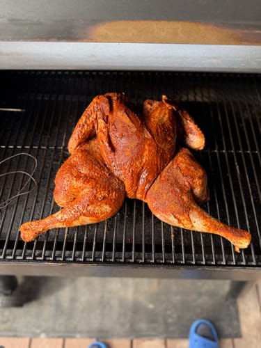 Reviewer's seasoned spatchcocked turkey cooking on a smoker grill, prepared using the Turkey Brine Kit.