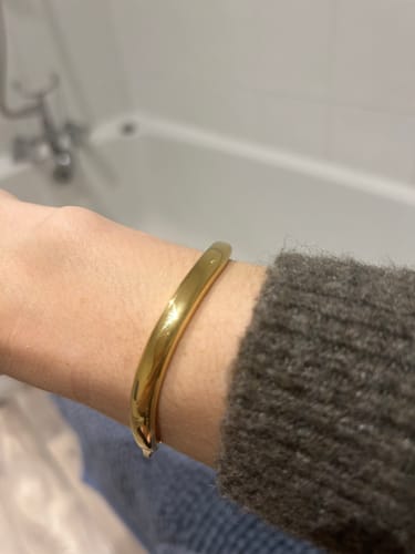 A customer's close-up of the shiny gold Wave Bangle on their wrist.
