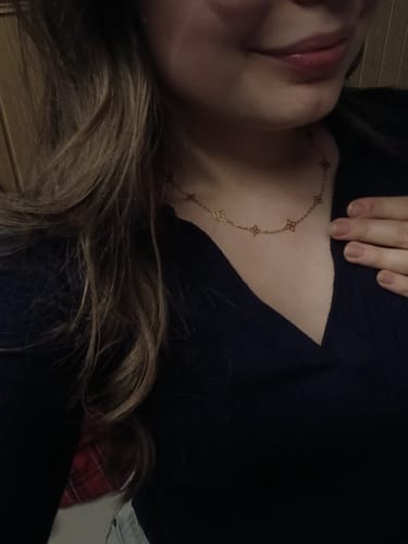 Nahaufnahme einer Rezensentin, die eine zarte goldene Halskette zu einem schwarzen Oberteil trägt.