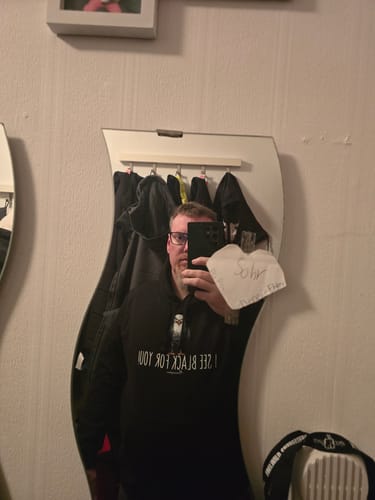 Ein Kunde zeigt die Passform des schwarzen „I see black for you“ Bio-Hoodies in einem Spiegelselfie.