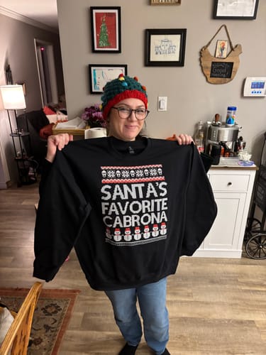 Reviewer holding up her black Santa's Favorite Cabrona sweatshirt to show the front graphic.