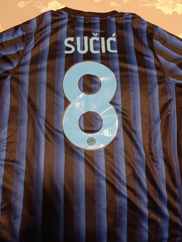 Recensore mostra il retro di una maglia da calcio a righe personalizzata con il nome SUČIĆ e il numero 8.