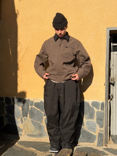 Reviewer standing outdoors wearing the coffee-colored Snow Jacket, adjusting the hem to show its boxy, modern fit.