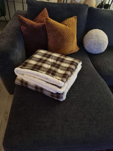 Kundens rutete sherpapledd ligger brettet sammen på en mørk sofa.