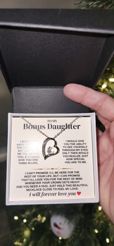Customer holds the open gift box, displaying the 'To My Bonus Daughter' heart necklace and its message card.