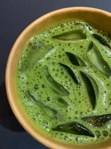 Gros plan sur le Thé Matcha Cérémonie Bio d'une cliente, servi glacé et mousseux dans un bol.