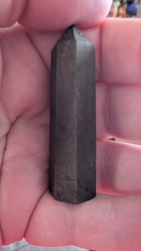 Close-up of a reviewer's hand holding a dark, pointed crystal from their VIP Crystal Club subscription.