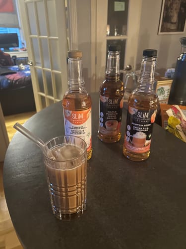 Un client montre trois sirops Slim Syrups de l'Édition Automne à côté d'un verre de café glacé.