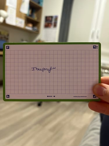 Client tenant une fiche de révision FLASH 2.0 quadrillée, avec le mot « Ibuprofen » écrit à la main au centre.
