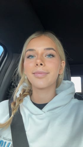 Customer selfie in a car, wearing a white hoodie. The product is not visible in this image.