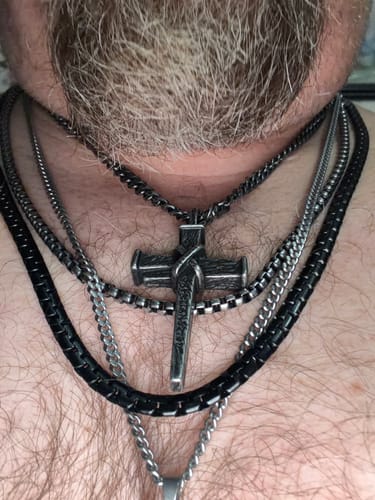 Close-up of a customer wearing the Nailed to the Cross necklace, layered with several other chains on their chest.