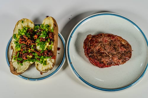 Customer's cooked USDA Prime Boneless Ribeye Steak plated next to a loaded baked potato.