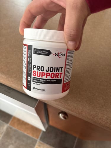 Un client tient dans sa main un flacon blanc de Pro Joint Support de XPN sur un comptoir de cuisine.