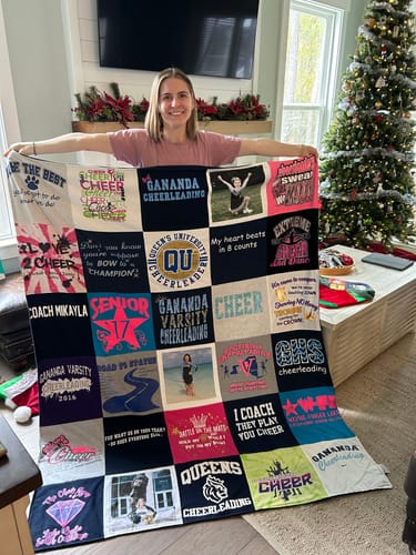 Customer holding up a large Premium T Shirt Quilt made from many colorful cheerleading t-shirts.